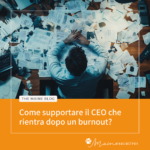 Vista dall’alto di una persona di spalle, con le mani appoggiate su una scrivania ingombra di fogli e documenti