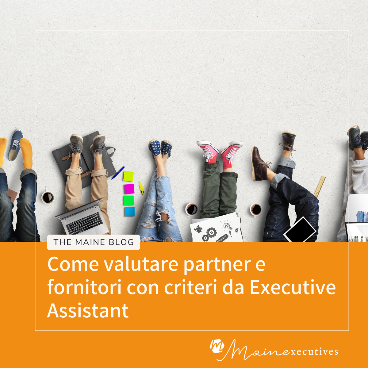 Inquadratura dall'alto delle gambe distese di più persone sedute a terra con scarpe diverse, laptop, quaderni, fogli, tablet, righello e tazze di caffè su sfondo chiaro